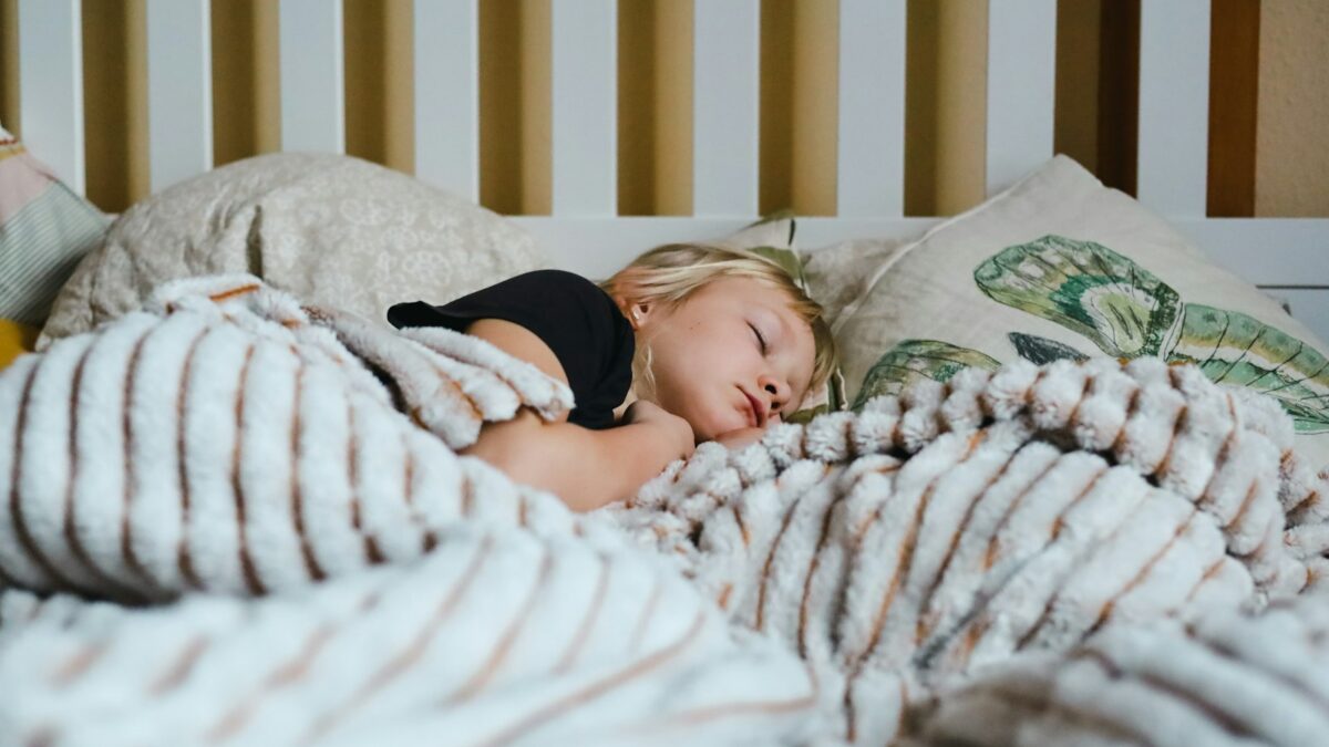 Anak kecil tidur nyenyak di kasur berselimut tebal, ilustrasi jam tidur anak yang cukup