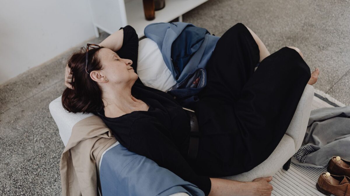 Wanita tidur siang sebentar di sofa ruang tamu dengan sepatu terlepas di lantai